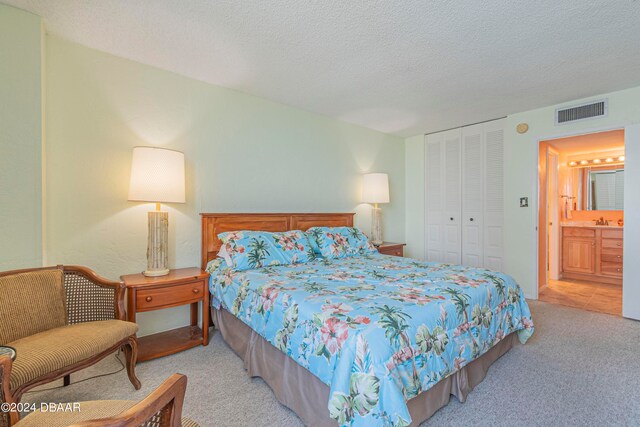 bedroom featuring ensuite bathroom, light colored carpet, a textured ceiling, and a closet