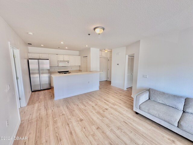 kitchen with stainless steel refrigerator, white cabinetry, a center island, and light hardwood / wood-style flooring