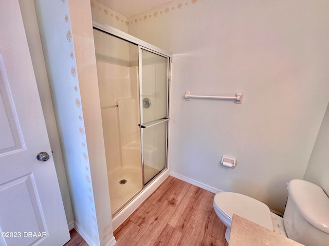 bathroom with hardwood / wood-style flooring, an enclosed shower, and toilet