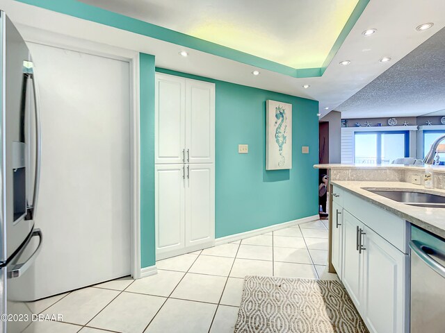 kitchen with sink, a textured ceiling, light tile patterned floors, white cabinets, and dishwasher