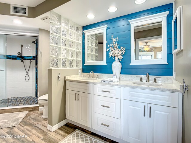 bathroom with wood-type flooring, toilet, a tile shower, vanity, and ceiling fan