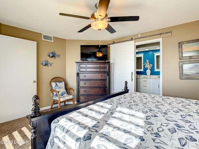 carpeted bedroom featuring a textured ceiling, a barn door, ceiling fan, and ensuite bath