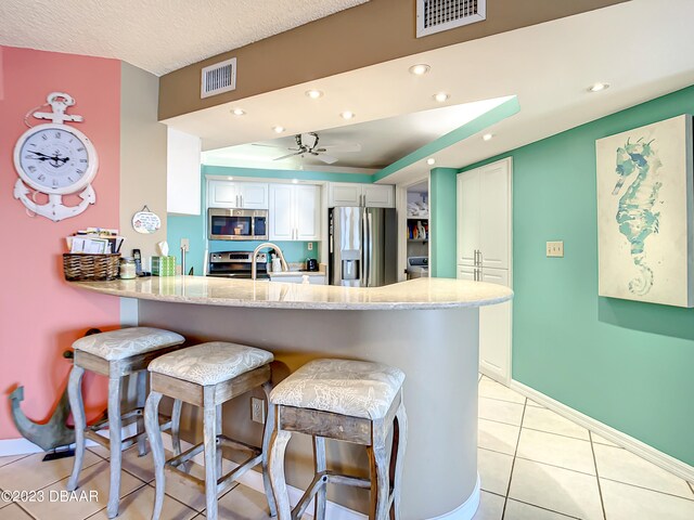 kitchen featuring stainless steel appliances, kitchen peninsula, a breakfast bar area, light tile patterned floors, and white cabinets