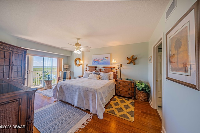 bedroom featuring access to exterior, visible vents, a textured ceiling, and wood finished floors