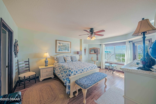 bedroom featuring ceiling fan, a textured ceiling, baseboards, and wood finished floors