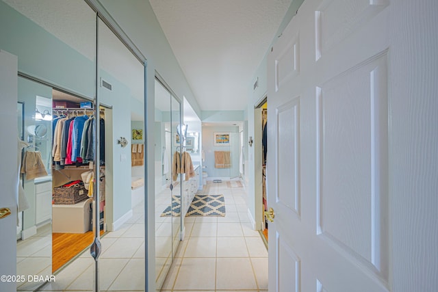 corridor featuring light tile patterned flooring, a textured ceiling, and baseboards