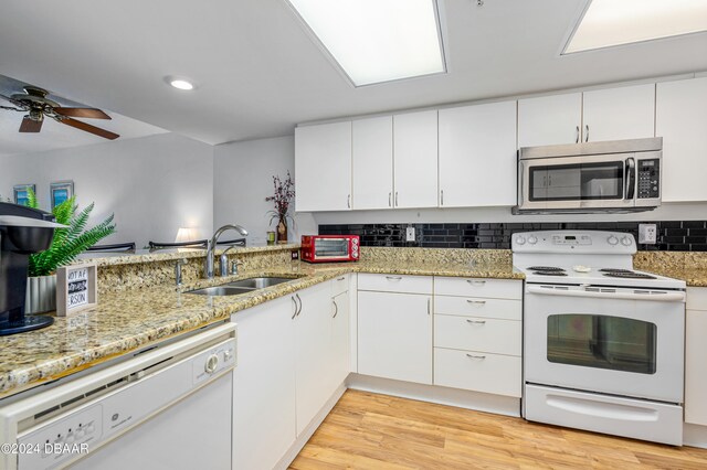 kitchen with light wood-type flooring, kitchen peninsula, sink, white cabinets, and white appliances