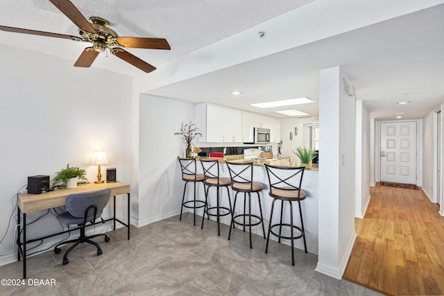 kitchen with kitchen peninsula, a textured ceiling, ceiling fan, a breakfast bar, and white cabinetry