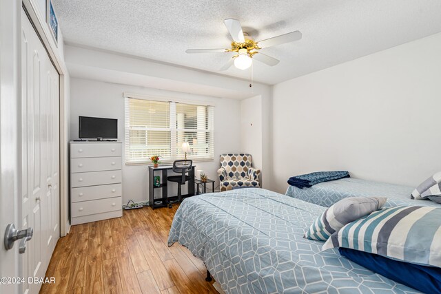 bedroom with a closet, hardwood / wood-style floors, ceiling fan, and a textured ceiling