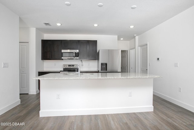 kitchen with light stone counters, sink, stainless steel appliances, and a kitchen island with sink