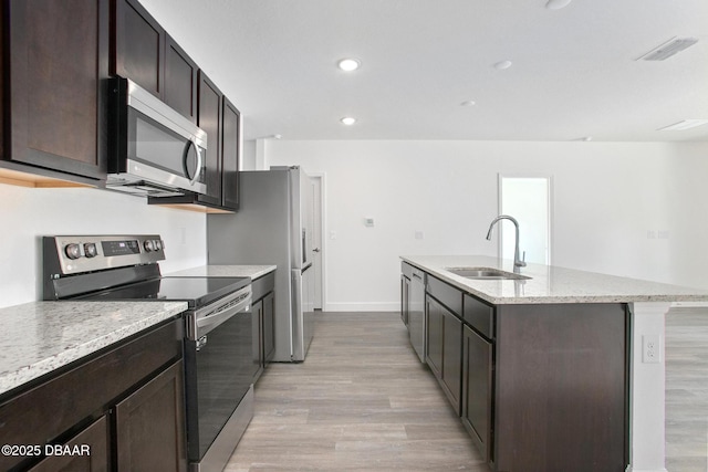 kitchen featuring dark brown cabinetry, stainless steel appliances, sink, light hardwood / wood-style floors, and an island with sink