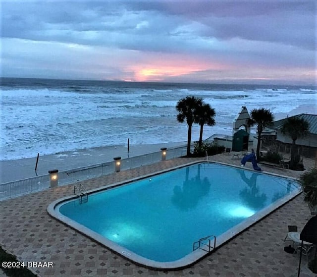 pool at dusk with a patio and a water view