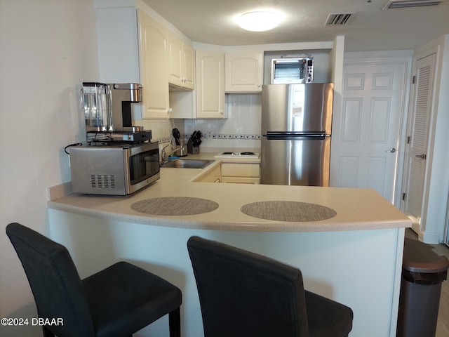 kitchen featuring sink, kitchen peninsula, appliances with stainless steel finishes, white cabinets, and decorative backsplash