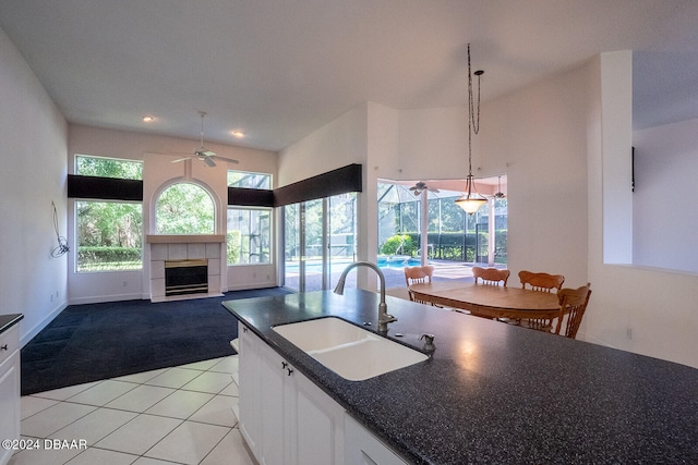 kitchen featuring white cabinets, sink, ceiling fan, a fireplace, and decorative light fixtures