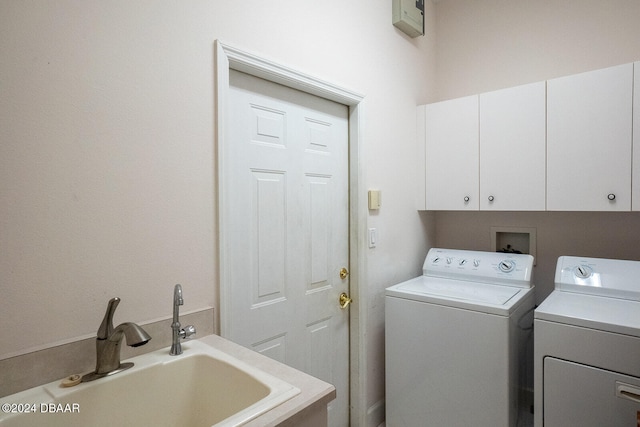 clothes washing area with washing machine and dryer, cabinets, and sink