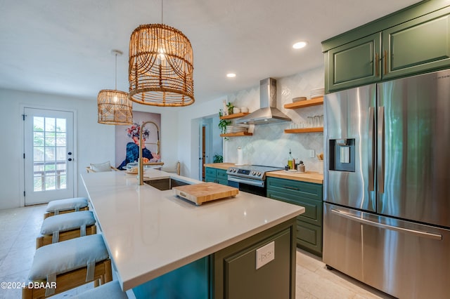 kitchen with appliances with stainless steel finishes, wall chimney exhaust hood, a breakfast bar area, and an island with sink