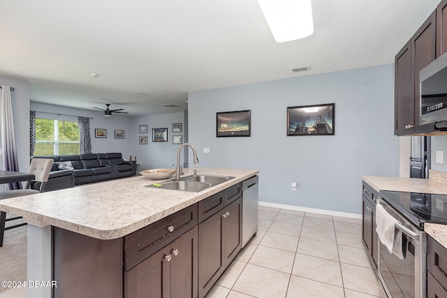 kitchen with sink, appliances with stainless steel finishes, light tile patterned floors, dark brown cabinets, and a kitchen island with sink