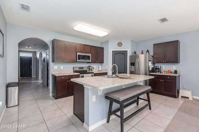 kitchen featuring appliances with stainless steel finishes, dark brown cabinets, sink, an island with sink, and a breakfast bar