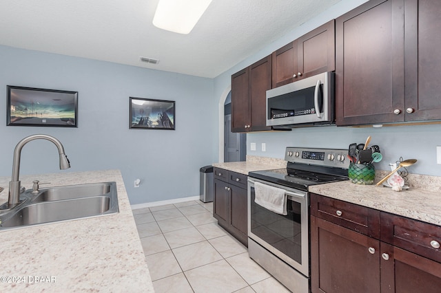 kitchen with dark brown cabinetry, a textured ceiling, sink, light tile patterned floors, and appliances with stainless steel finishes