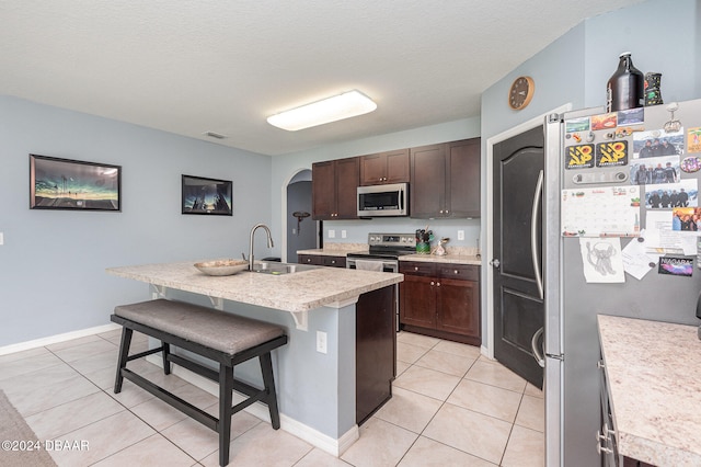 kitchen featuring a center island with sink, a textured ceiling, sink, a breakfast bar area, and appliances with stainless steel finishes