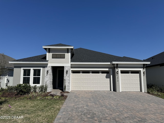 prairie-style house featuring stone siding, driveway, roof with shingles, and an attached garage