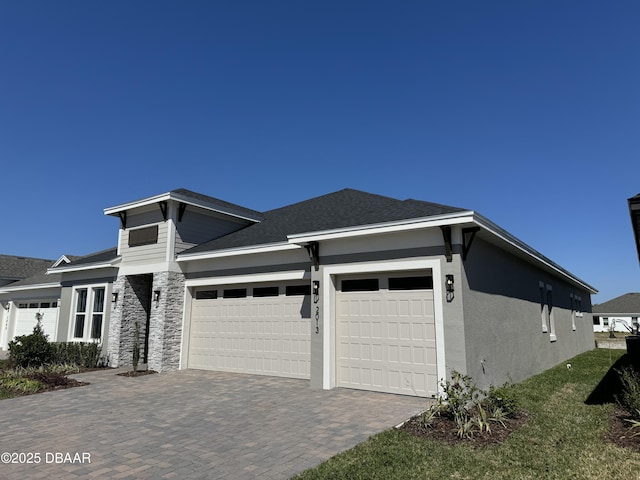 view of front of home with stucco siding, a shingled roof, decorative driveway, and a garage