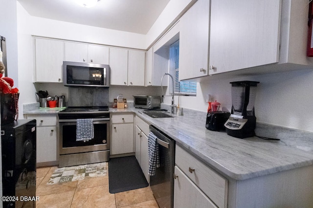 kitchen with light tile patterned floors, stainless steel appliances, a sink, white cabinets, and light countertops