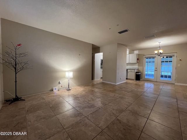 unfurnished living room with a textured ceiling, a textured wall, visible vents, and an inviting chandelier