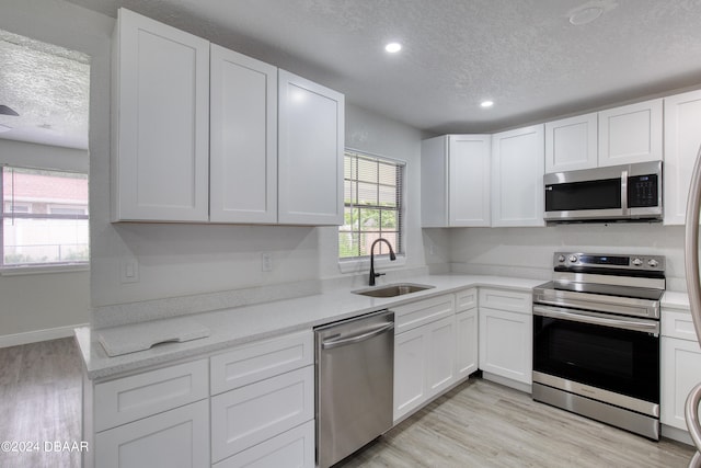 kitchen featuring stainless steel appliances, white cabinets, a textured ceiling, sink, and light hardwood / wood-style flooring