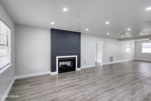 unfurnished living room with a large fireplace, ceiling fan, a textured ceiling, and light wood-type flooring