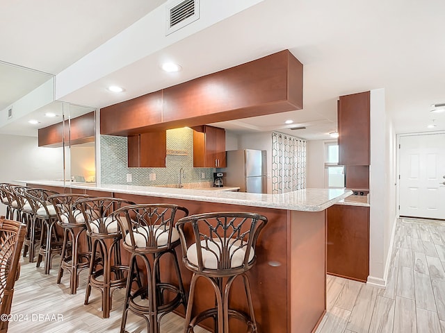 kitchen featuring tasteful backsplash, stainless steel fridge, light wood-type flooring, a breakfast bar, and kitchen peninsula