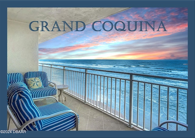 balcony at dusk featuring a beach view and a water view