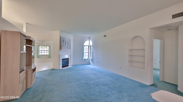 unfurnished living room with ceiling fan, a healthy amount of sunlight, built in features, and carpet flooring