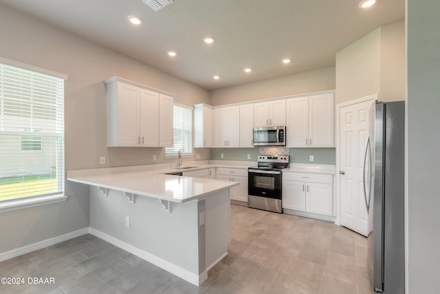 kitchen featuring white cabinets, kitchen peninsula, a healthy amount of sunlight, and stainless steel appliances