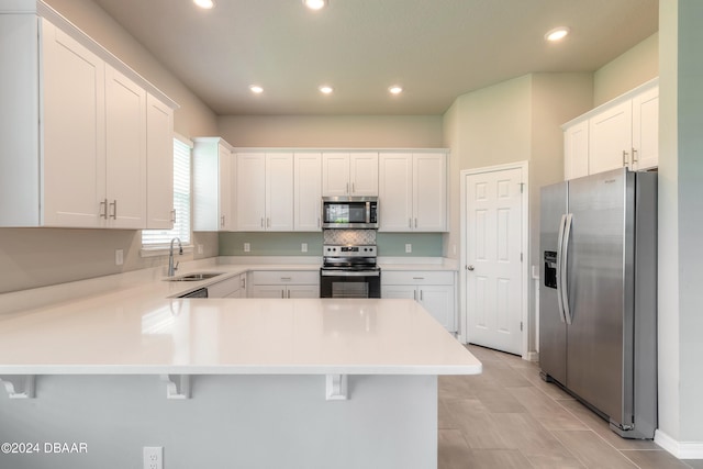 kitchen with appliances with stainless steel finishes, a kitchen bar, sink, white cabinets, and kitchen peninsula