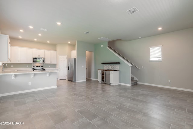 kitchen featuring appliances with stainless steel finishes, sink, a breakfast bar, white cabinets, and beverage cooler