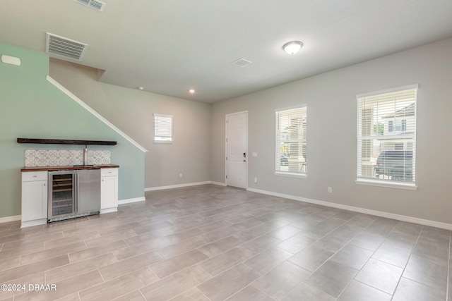 unfurnished living room featuring beverage cooler and bar