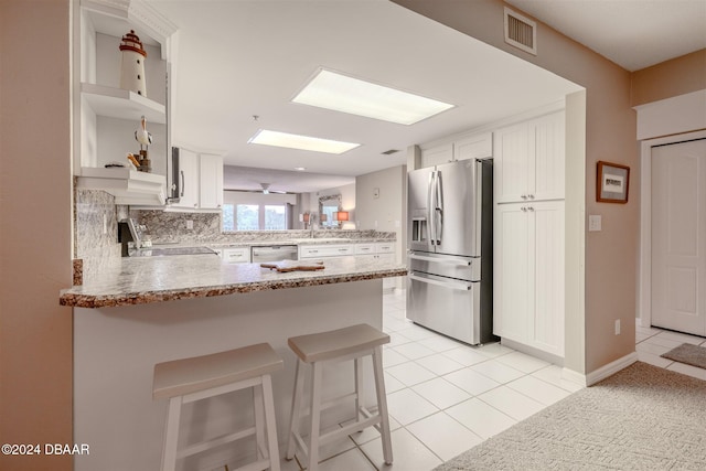 kitchen with kitchen peninsula, appliances with stainless steel finishes, a kitchen breakfast bar, white cabinets, and light tile patterned flooring