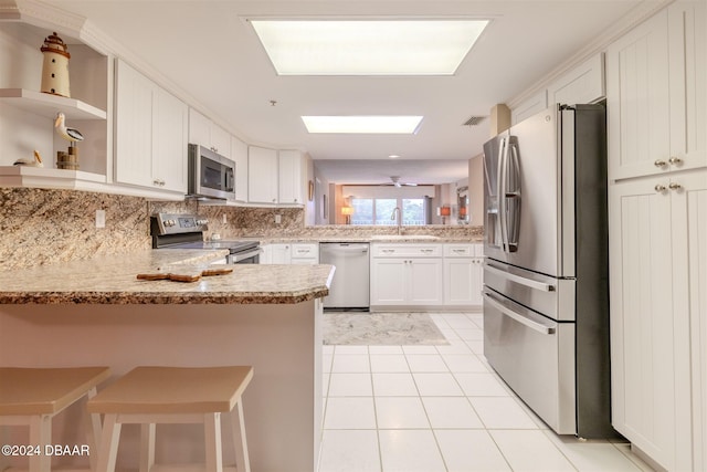 kitchen with kitchen peninsula, light tile patterned floors, appliances with stainless steel finishes, white cabinetry, and a breakfast bar area