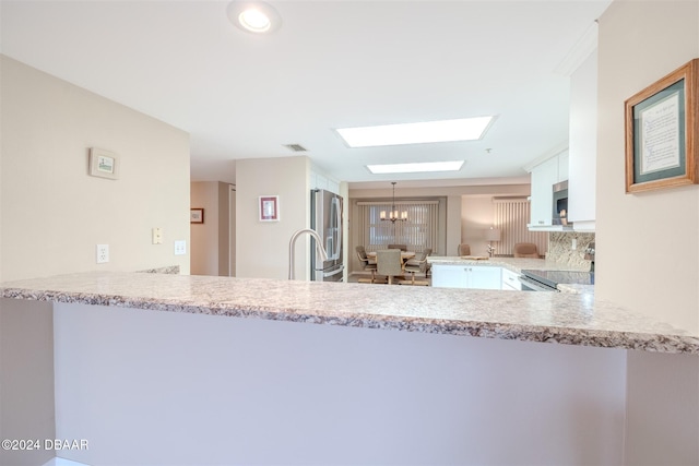 kitchen with a skylight, kitchen peninsula, decorative light fixtures, white cabinets, and appliances with stainless steel finishes