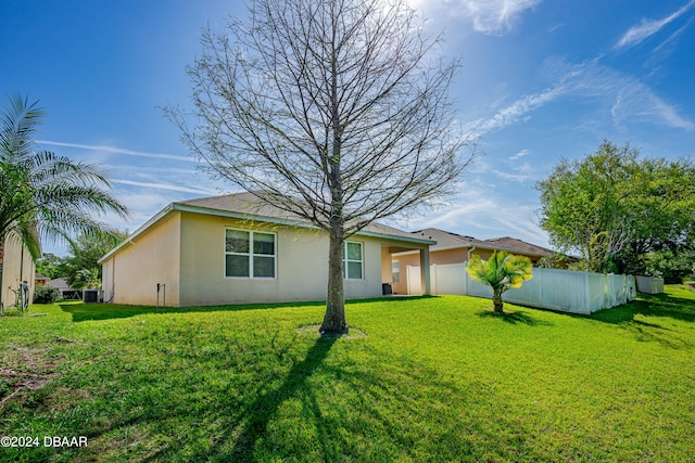 rear view of property featuring central air condition unit and a lawn