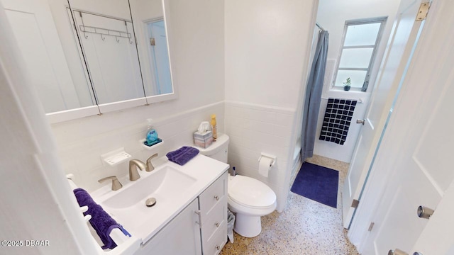 full bathroom featuring a shower with shower curtain, a wainscoted wall, speckled floor, tile walls, and toilet