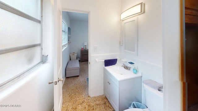 bathroom featuring tile walls, wainscoting, vanity, and speckled floor