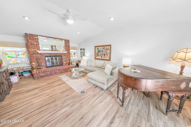 living room featuring a fireplace, light hardwood / wood-style flooring, ceiling fan, and vaulted ceiling