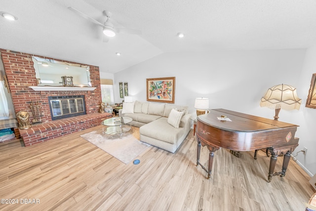 living room featuring vaulted ceiling, a textured ceiling, ceiling fan, a fireplace, and light hardwood / wood-style flooring