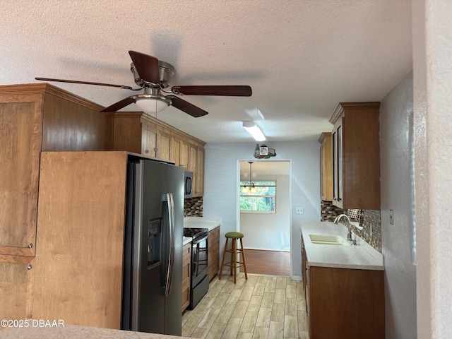 kitchen with sink, decorative backsplash, a textured ceiling, light hardwood / wood-style floors, and stainless steel appliances