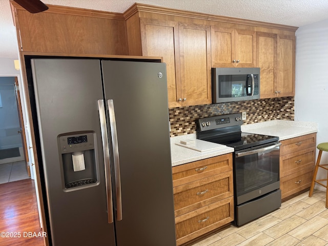 kitchen featuring decorative backsplash, stainless steel appliances, a textured ceiling, and light hardwood / wood-style floors