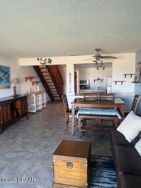 living room with a ceiling fan, stairway, and a textured ceiling