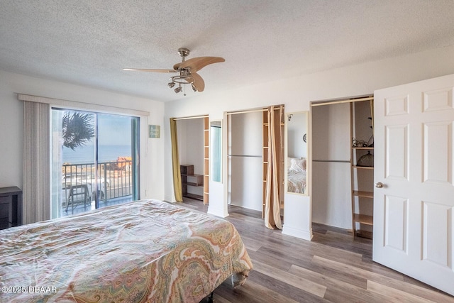 bedroom featuring light hardwood / wood-style flooring, ceiling fan, access to exterior, a textured ceiling, and multiple closets