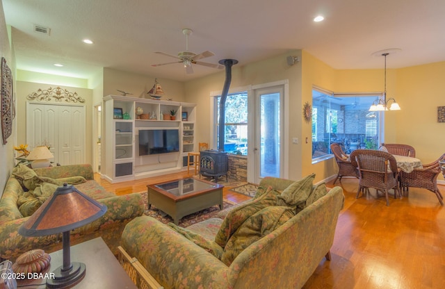 living room with ceiling fan with notable chandelier, hardwood / wood-style floors, and a wood stove